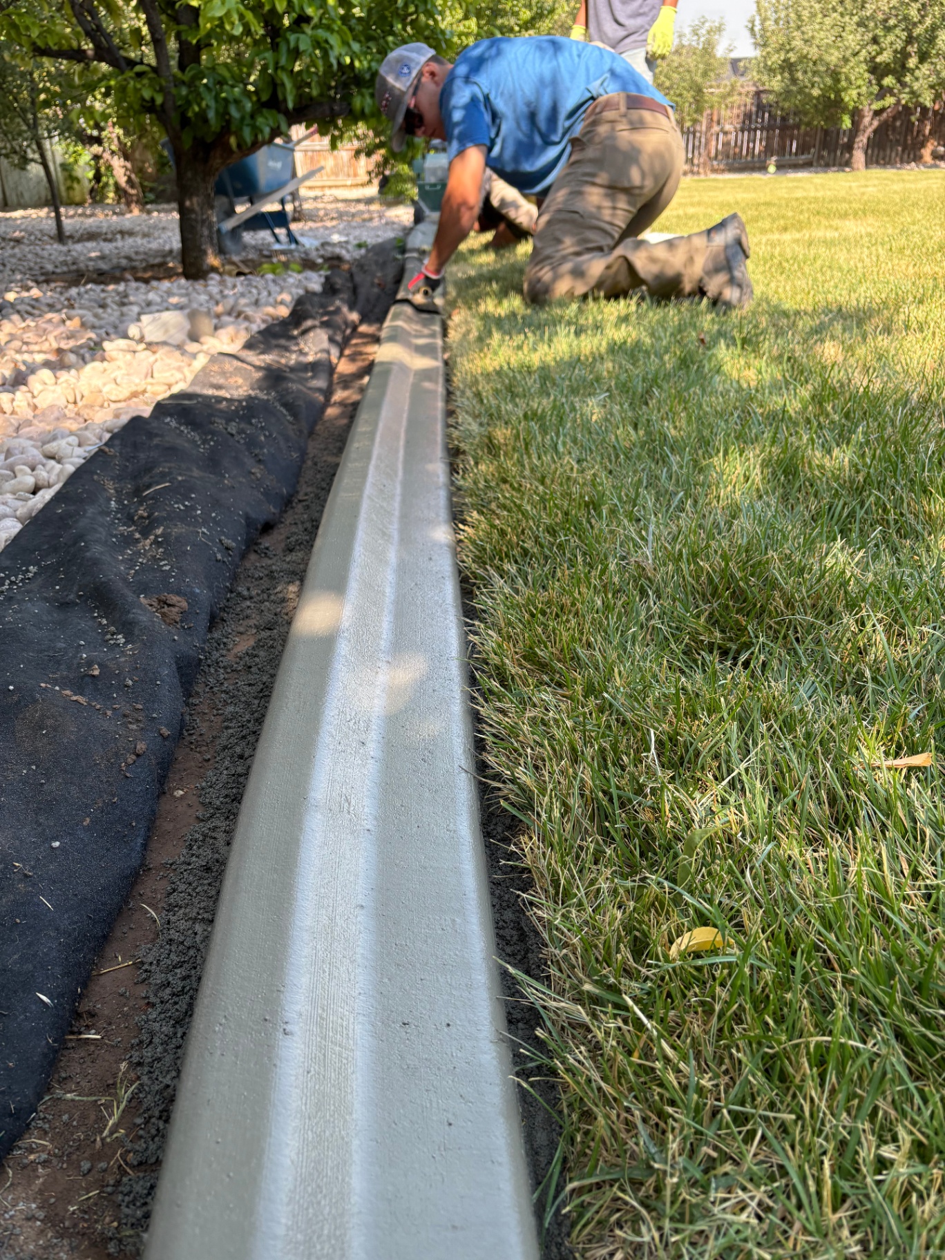 Blue Wing Construction and Landscape crew member hand-troweling a freshly extruded continuous concrete landscape curb during install.