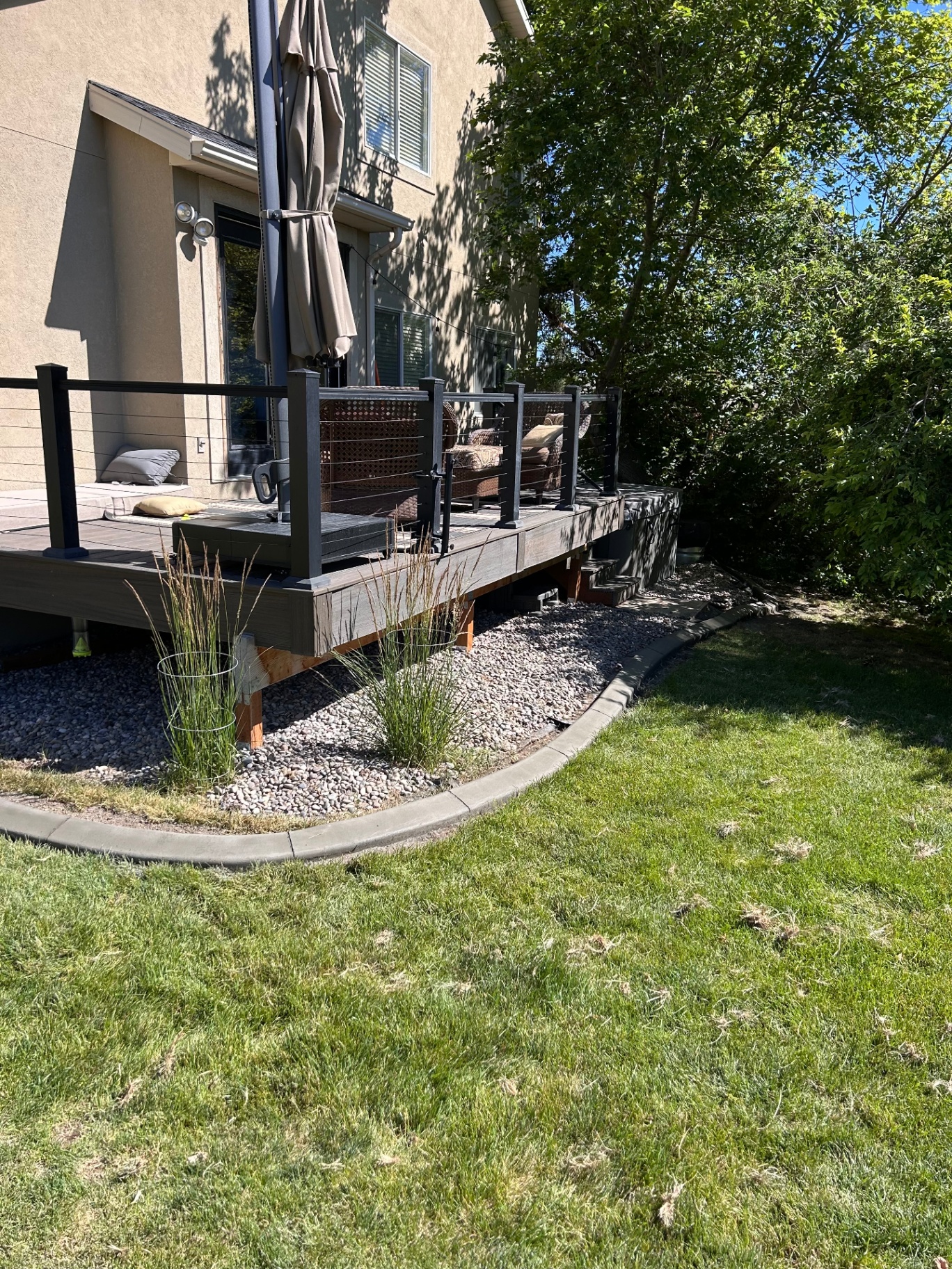 Curved concrete curbing separating a river-rock drainage bed from a lush green lawn beside a residential deck in Utah.