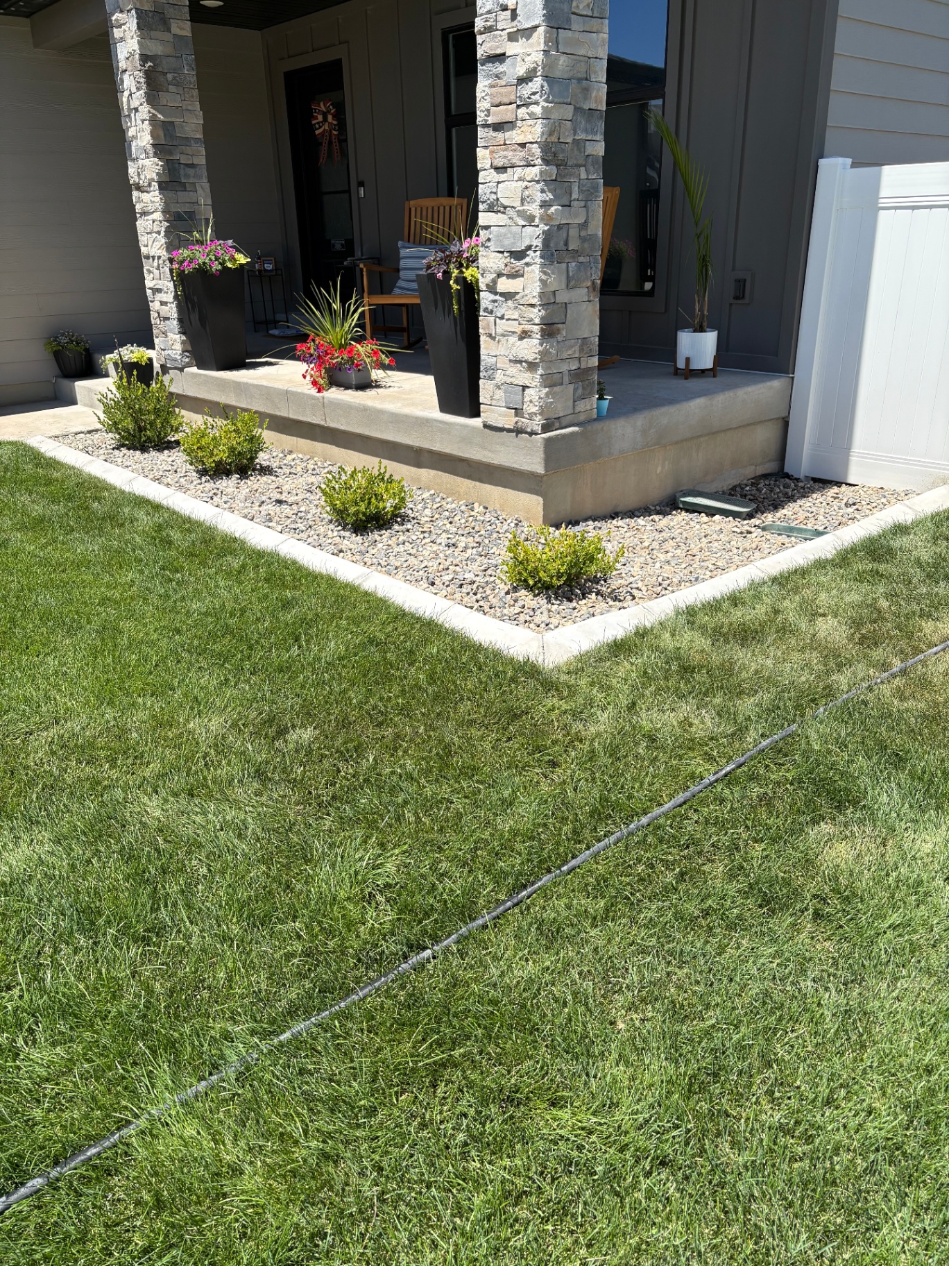 Fresh green lawn with clean white concrete curbing edging a stone-column front-porch flower bed, installed by Blue Wing Construction and Landscape.