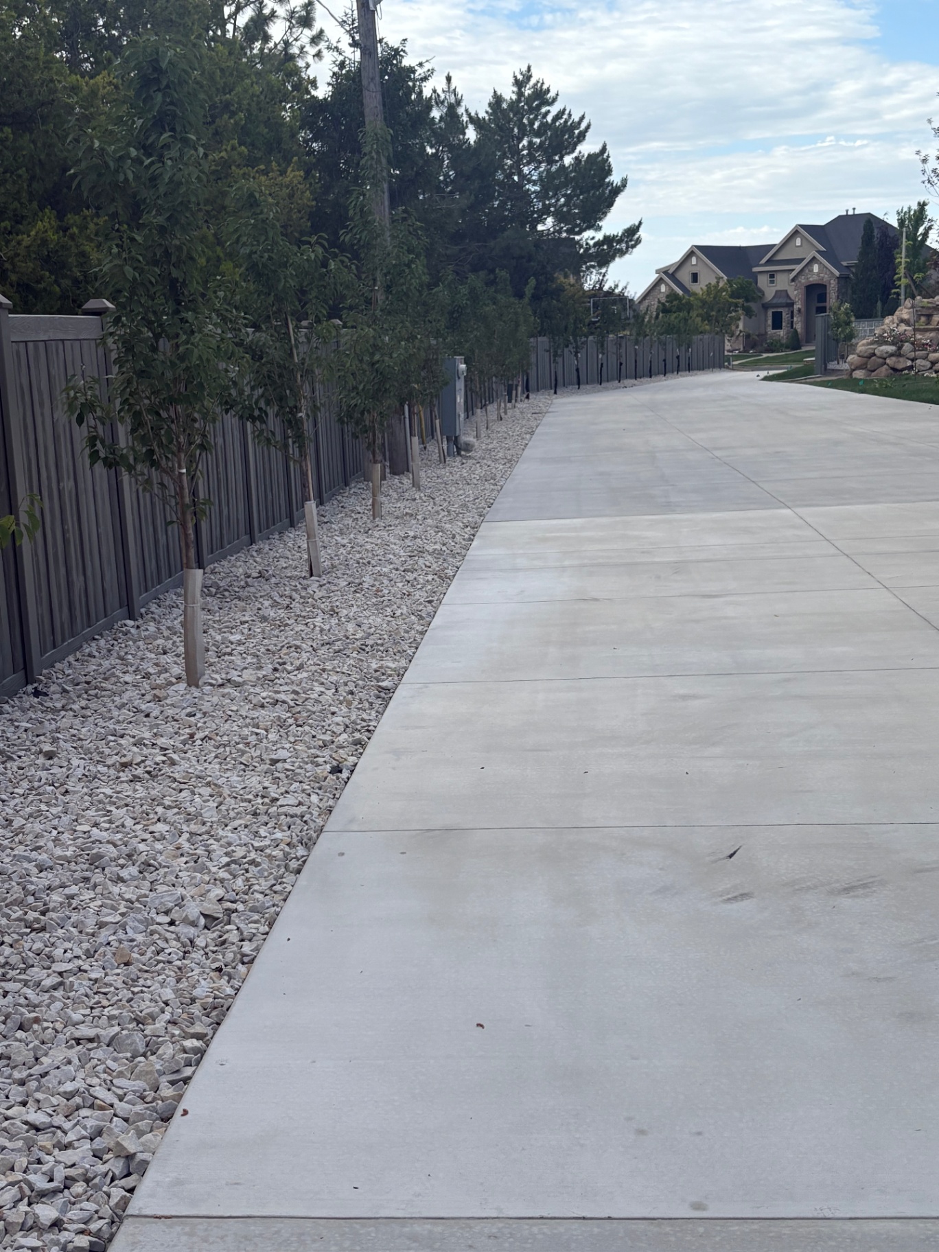 Wide broom-finish concrete driveway bordered by white decorative rock landscaping and young trees at a Utah home.