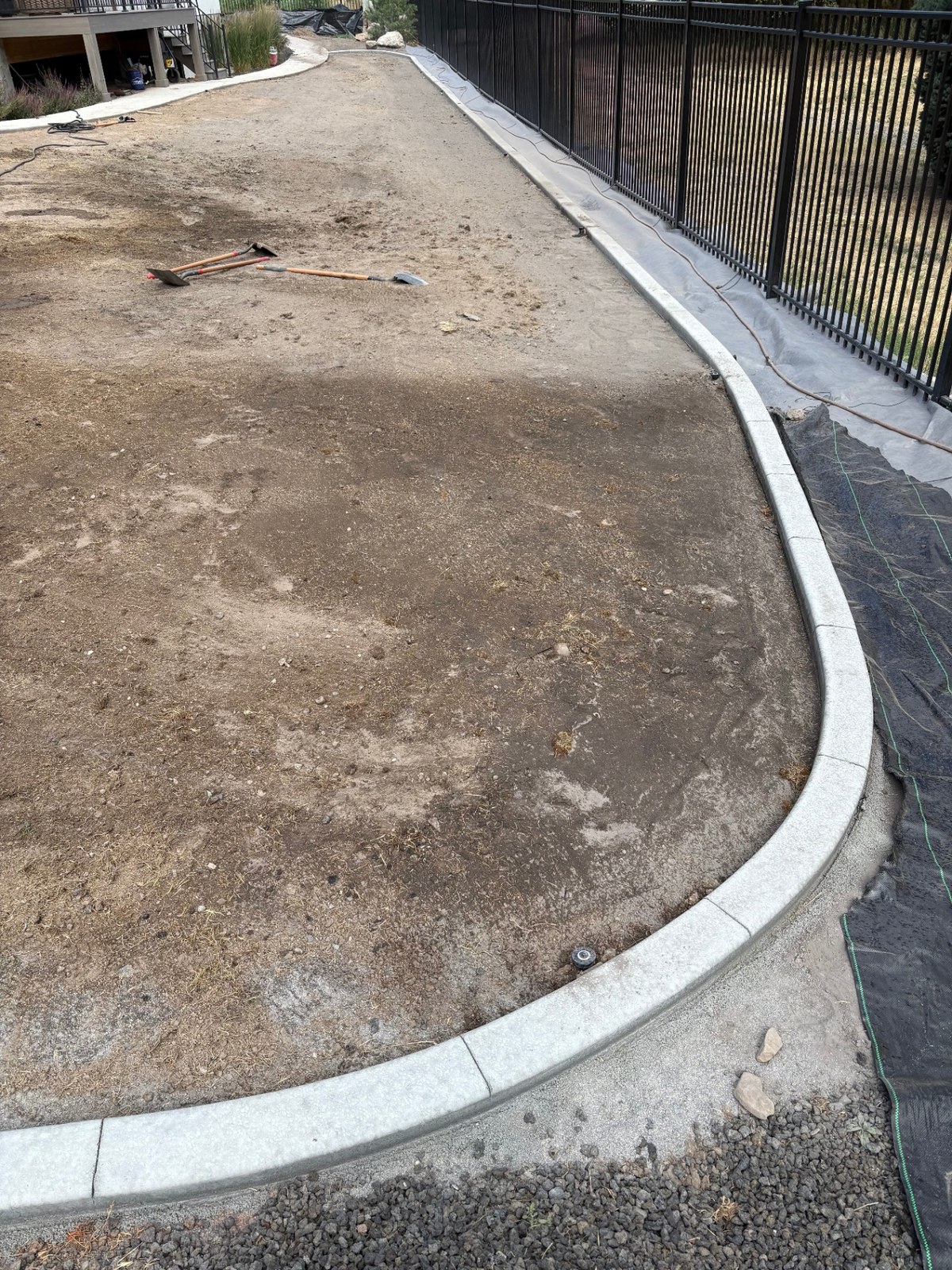 Before photo of a Utah backyard: bare dirt yard with freshly extruded white concrete curbing lining a black metal fence, awaiting sod and landscaping by Blue Wing Construction and Landscape.